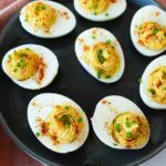Deviled eggs topped with smoked paprika and chopped chives on a serving platter.