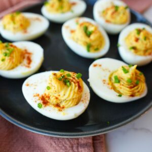 Deviled eggs topped with smoked paprika and chopped chives on a serving platter.