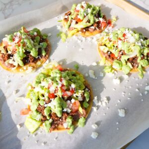 Ground beef tostadas topped with refried beans, lettuce, tomatoes, onions, queso fresco and cilantro lime sauce.
