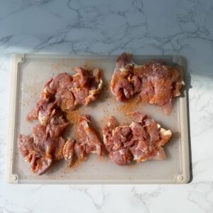 Chicken with seasoning on a cutting board.