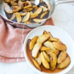 Southern fried apples in a skillet and on a plate, coated in a glossy cinnamon sugar butter sauce.