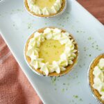 Mini key lime pies in graham cracker crusts topped with whipped cream and lime zest.