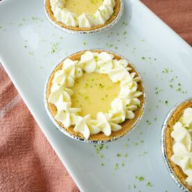 Mini key lime pies in graham cracker crusts topped with whipped cream and lime zest.