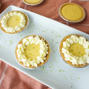Mini key lime pies in graham cracker crusts topped with whipped cream and lime zest.