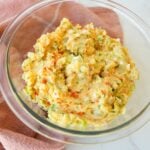 Creamy potato salad in a bowl with chopped eggs, herbs, celery, and smoked paprika on top.