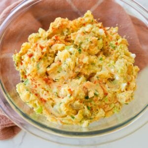 Creamy potato salad in a bowl with chopped eggs, herbs, celery, and smoked paprika on top.