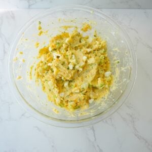 Creamy potato salad in a bowl with chopped eggs, herbs and celery.