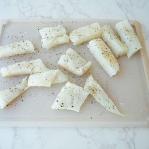 Fish cut up in pieces on a cutting board with salt and pepper.