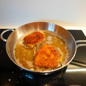 Fish frying in a silver pan.