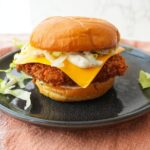 Crispy fried cod sandwich on a toasted bun with melted American cheese, shredded lettuce, and tartar sauce.
