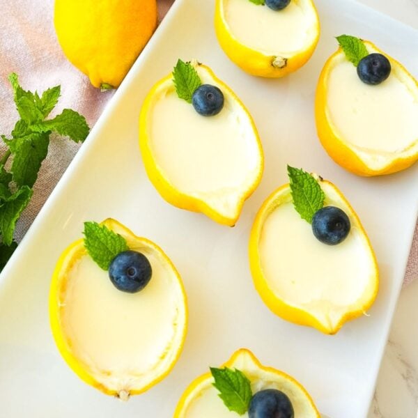 Lemon posset served inside hollowed lemon cups with blueberries on top.