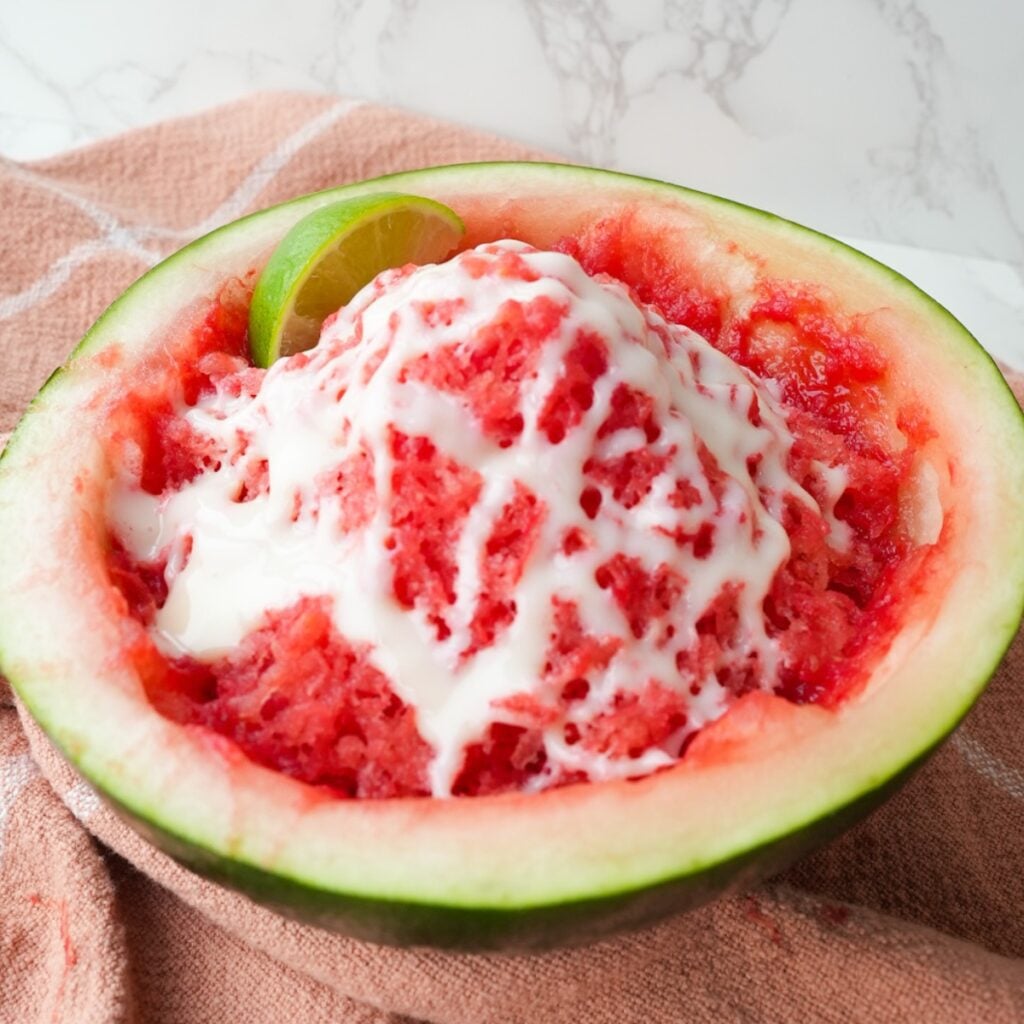 Shaved watermelon ice served in a watermelon half with lime juice and sweetened condensed milk drizzled on top.