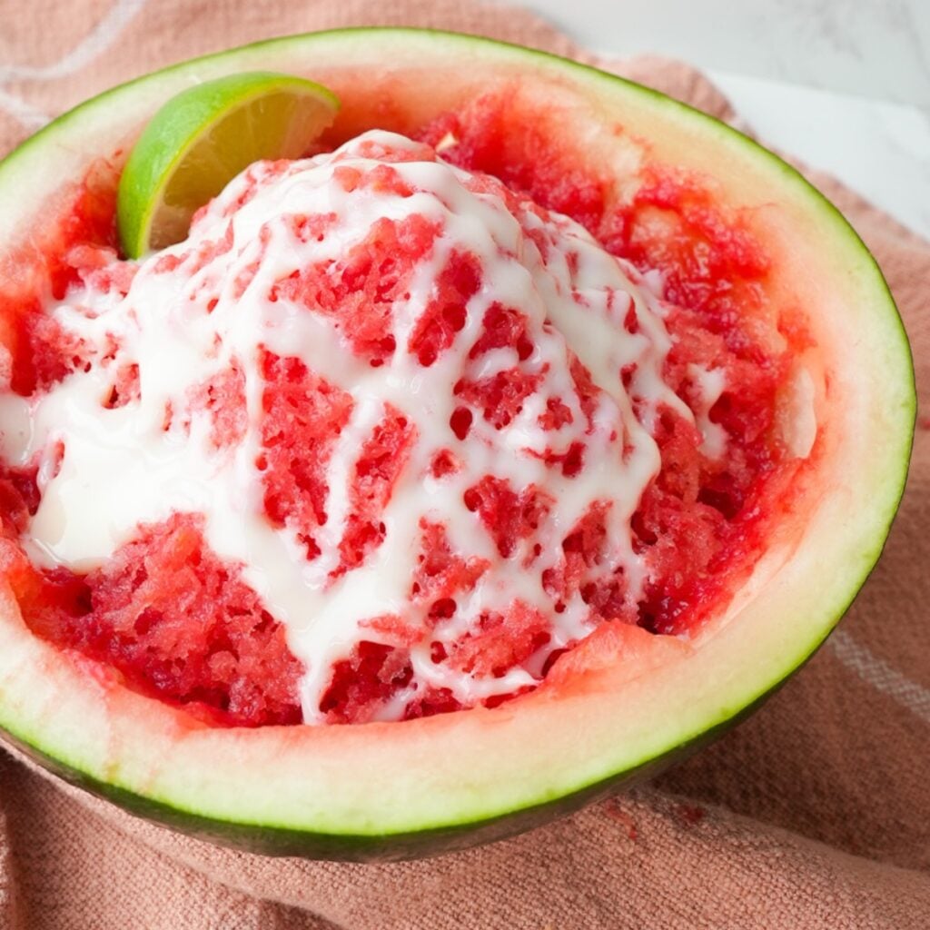 Shaved watermelon ice served in a watermelon half with lime juice and sweetened condensed milk drizzled on top.