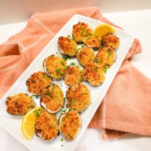 Baked littleneck clams topped with golden panko breadcrumbs, parsley, and lemon wedges on the side.