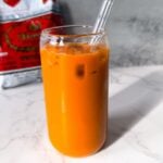Thai iced tea poured over ice with sweetened condensed milk and evaporated milk swirled through the glass.
