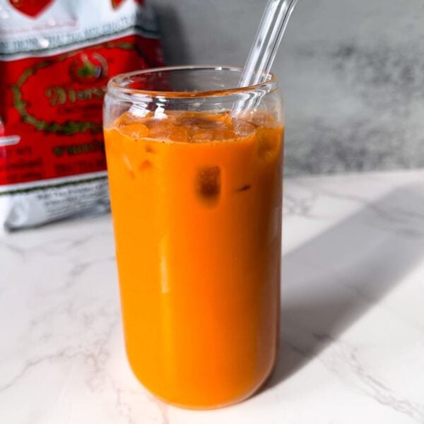 Thai iced tea poured over ice with sweetened condensed milk and evaporated milk swirled through the glass.