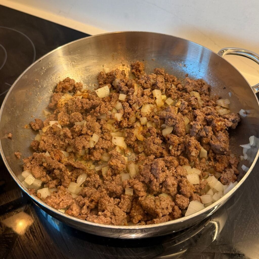 Seasoned ground beef in a pan with diced onions.