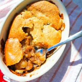 Warm apple cobbler with cinnamon-spiced apples and a golden baked topping in a small baking dish.