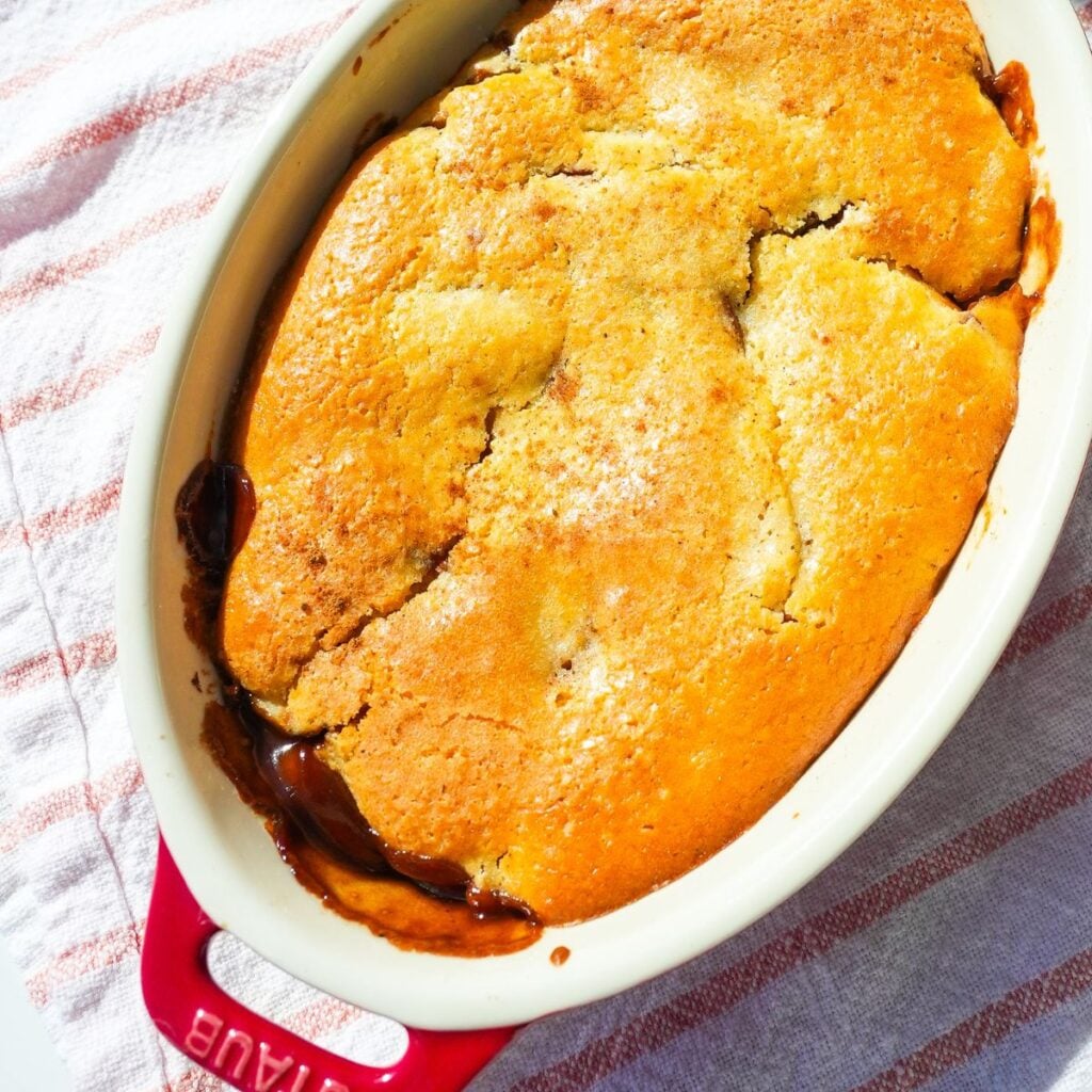 Warm apple cobbler with cinnamon-spiced apples and a golden baked topping in a small baking dish.