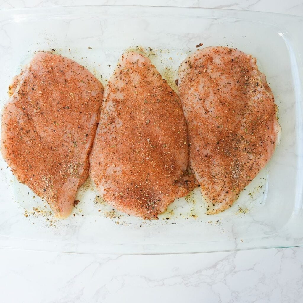 Chicken breast seasoned in a glass baking dish before cooking.
