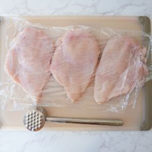 Chicken breast pounded on a cutting board with a mallet.