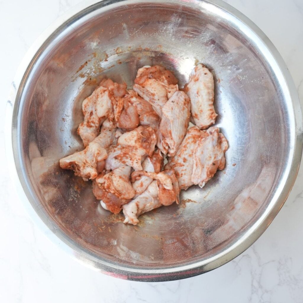 Raw chicken wings in a bowl with seasoning.