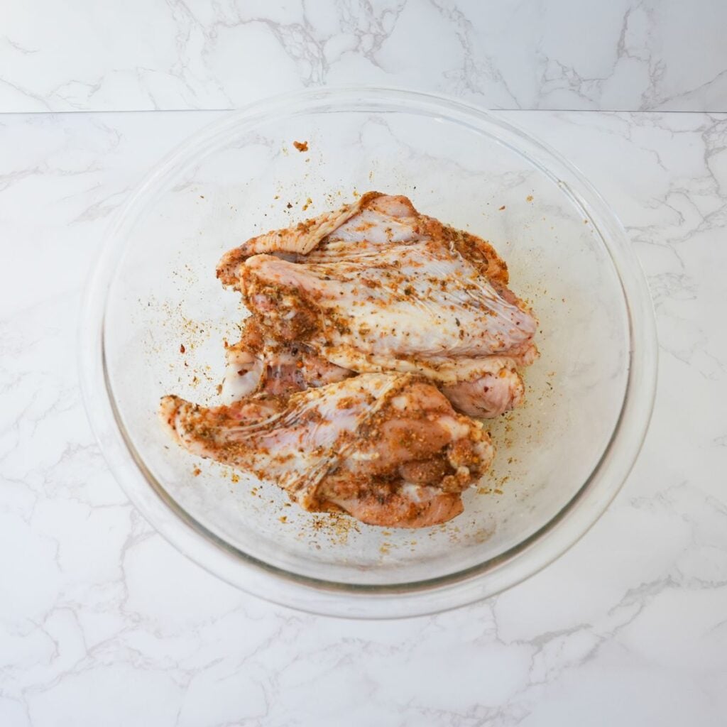 Turkey wings in a glass bowl with seasonings.